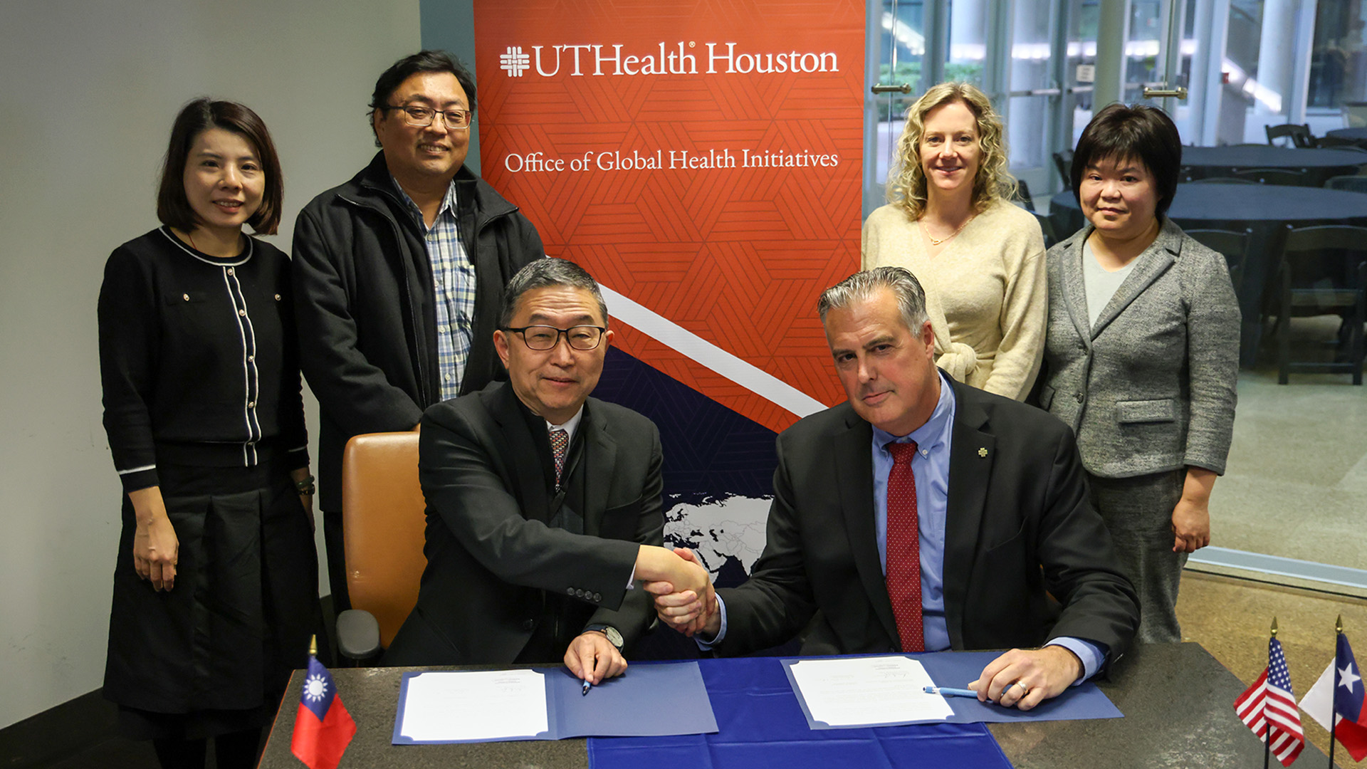 Six people sitting and standing behind a table with a UTHealth Houston backdrop behind them.